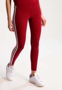 Röda leggings i elastiskt material med vita sidestreck och en liten logotyp. Matcher med vita sneakers med blå accenter.