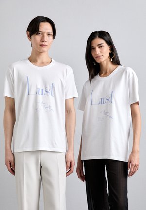 T-shirt unisex in cotone bianco con la scritta "Lust" stampata in blu chiaro, con testo curvo e accenti distintivi. Vestibilità ampia.