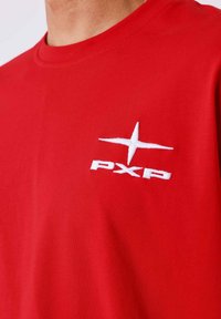 T-shirt in cotone rosso con collo a giro e logo ricamato "PXP" bianco con design a stella nella zona del petto sinistro.