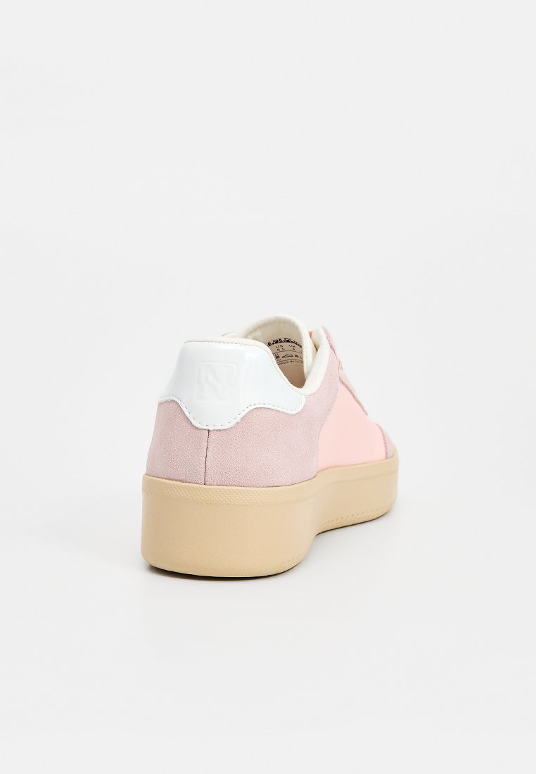 Zapatilla de ante rosa y beige con talón de goma blanco, punta redonda y suela marrón claro. Presenta una textura suave y un diseño minimalista.