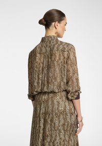 Abito in stampa leopardata con vestibilità ampia, maniche lunghe arrotolate ai polsini e colletto. Il materiale sembra liscio con una trama fluida.