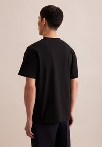 T-shirt in cotone nero con colletto a giro e maniche corte, mostrato da dietro. Texture liscia con vestibilità comoda.