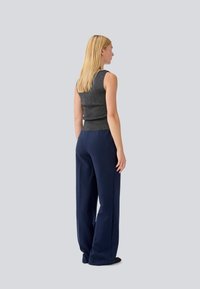 Gray sleeveless top paired with dark blue wide-leg trousers, featuring a smooth texture and relaxed fit. The background is neutral gray.