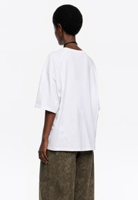 Camiseta de algodón blanca con un corte relajado y mangas cortas. Presenta un escote redondo y un detalle de costura mínima, lo que proporciona una textura suave.