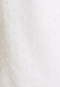 Tissu blanc avec une texture pointillée subtile présentant de petits points en relief répartis uniformément sur la surface.