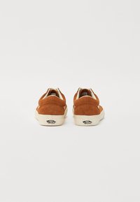 Baskets basses en daim marron avec une semelle en caoutchouc crème, présentant un détail de logo sur le talon et un design de bout arrondi.