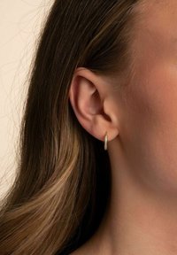 Guldörhänge i form av en ring med en strukturerad yta och små inslagna klara stenar. Designen är cirkulär och reflekterar ljus på olika sätt.