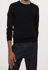 Svart stickad tröja med rund halsringning och långa ärmar, med ribbade muddar och nederkant. Matchad med mörka denimjeans.