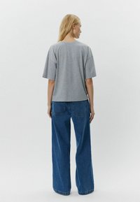 Camiseta gris de manga corta con un corte holgado, combinada con vaqueros de pierna ancha azul de talle alto que tienen dos bolsillos traseros.