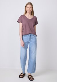 T-shirt bordeaux a manica corta con scollo a V abbinato a jeans larghi azzurri e sandali neri con dettagli a catena.