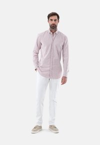 Camicia da uomo a maniche lunghe a righe rosa chiaro e bianche, con taschino sul petto, abbinata a pantaloni bianchi e scarpe beige.