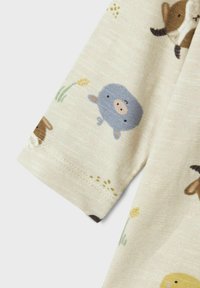 Beige bomullstyg med en mjuk textur, med illustrationer av djur och blommor i dämpade färger, visade på en kortärmad blus.