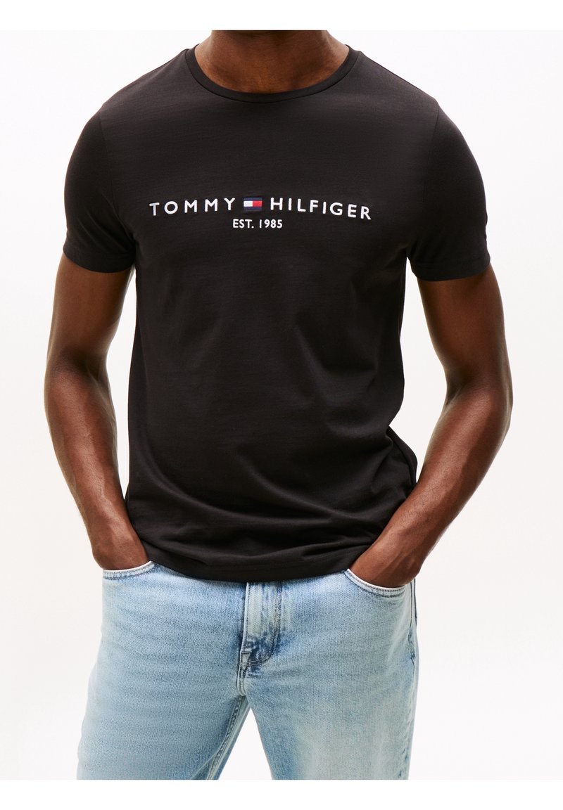 Czarny bawełniany T-shirt z białym haftowanym logo "TOMMY HILFIGER EST. 1985", dopasowany krój, okrągły dekolt, gładka tekstura.