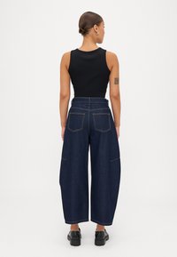 Top negru fără mâneci, asortat cu blugi din denim închis, cu talie înaltă și picioare largi, având buzunare la spate și detalii de cusătură deschisă.