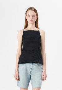 Zwarte fitted mouwloze top met een vierkante halslijn en geplooide textuur, gecombineerd met lichtblauwe denim shorts voor contrast.