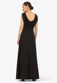 Black maxi dress with a draped cowl neckline and an open back, featuring a fitted bodice and flowing skirt. Made of smooth fabric.