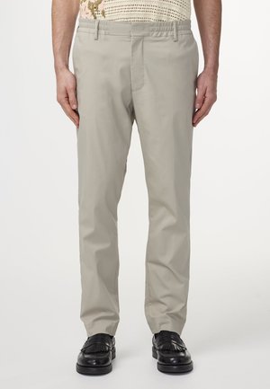Lichtgrijze, op maat gemaakte broek met een elastische tailleband, een aantal voorzakken en een gladde, matte textuur, gecombineerd met zwarte, gestructureerde nette schoenen.
