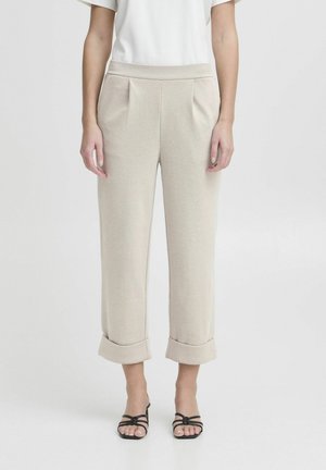 Beige Hose aus strukturiertem Stoff, mit einem taillierten Bund, Falten und umgekrempelten Säumen. Kombiniert mit einfachen schwarzen Riemchensandalen.