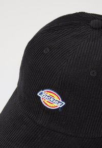 Fekete kordbársony sapka, kerek hímzett Dickies logóval, piros, sárga és kék elemekkel, struktúrált formával és felső gomb részlettel.