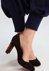 Hnědé semišové lodičky na vysokém podpatku s průhledným želvovinovým blokovým podpatkem. Podpatek má hladký povrch, který poskytuje stabilitu a podporu.