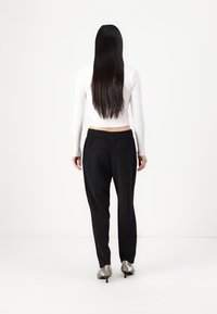 Pantaloni neri a gamba asciutta con cintura elastica, abbinati a un top aderente bianco a coste, visti da dietro, che mettono in risalto il design elegante e la silhouette.