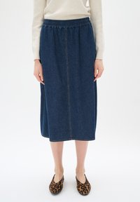 Denim midi krilo z elastičnim pasom, temno modre barve, vertikalni šivi, gladka tekstura, v kombinaciji z obutvijo v leopardjem vzorcu.