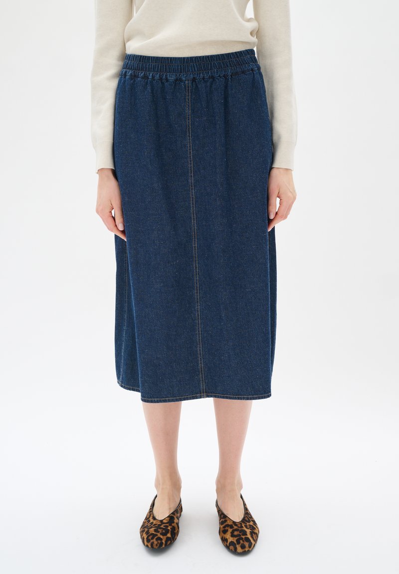 Denim midi krilo z elastičnim pasom, temno modre barve, vertikalni šivi, gladka tekstura, v kombinaciji z obutvijo v leopardjem vzorcu.