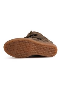 Καφέ μπότες από σουέντ ξαπλωμένες στο πλάι που δείχνουν την υφασμένη λαστιχένια σόλα με γεωμετρικό μοτίβο λαβής και ραφές.