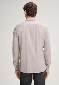 Camicia a maniche lunghe grigia chiara con righe verticali. Presenta un colletto, polsini con bottone e un piccolo logo sulla manica sinistra.