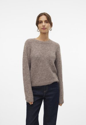 Pull en tricot brun duveteux avec des manches longues, un col rond et une coupe décontractée, associé à un jean en denim bleu foncé. Texture douce, design minimal.