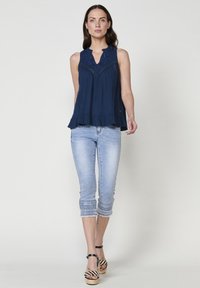 Top senza maniche blu navy con design ricamato e orlo a balze, abbinato a capri in denim chiaro con cuciture decorative sui polsini.