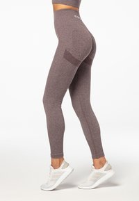 Leggings en una tela texturizada de color burdeos con cintura alta, que presentan un diseño de panel lateral y costuras de acento. Combinados con zapatillas deportivas blancas.
