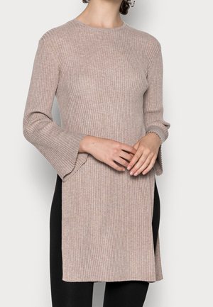 Pull en tricot côtelé beige avec un col rond, des manches longues évasées et des fentes sur les côtés. Le tissu est texturé, avec une silhouette ajustée.