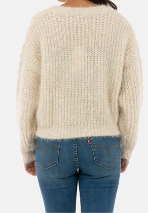 Person wearing a fluffy cream knit sweater and blue denim jeans shown from the back against a plain background.