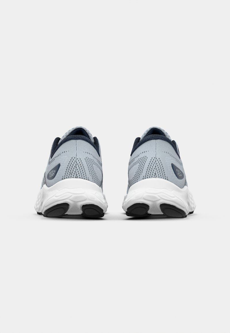 Zapatillas deportivas de color gris claro con parte superior de malla, acentos en azul oscuro contrastantes y suela texturizada blanca. Presentan un collar y un talón acolchados.