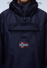 Chaqueta impermeable de color navy con un alto collar, bolsillo frontal con cremallera y acentos de velcro, que presenta un parche de la bandera noruega en rojo, blanco y azul.