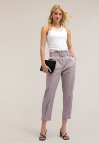 Lichtpaarse hoge taillebroeken met een riem en geplooide details, gecombineerd met een witte tanktop. Inclusief zwarte clutch en sandalen met banden.