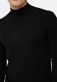 Schwarzer Rollkragenpullover aus weichem Strickstoff. Hat ein tailliertes Design mit hohem Kragen und langen Ärmeln. Glatte Textur.