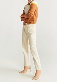 Brązowo-biały dziergany sweter, kremowe proste dżinsy oraz beżowe wysokie buty na obcasie. Sweter ma okrągły dekolt i teksturowany wzór.