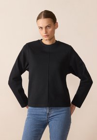 Svart langermet genser med rund hals, med en glatt tekstur og en enkel skjæring. Kombinert med lyseblå denimjeans.