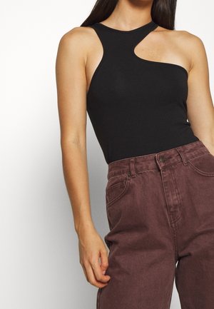 Sort ærmeløs bodystocking med et unikt asymmetrisk udskåret snit ved skulderen, kombineret med vinrøde bukser med højt talje. Glat tekstur.