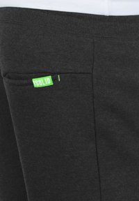 Pantaloni de trening gri închis, cu o textură netedă, având un mic eticheta verde cu textul "!SOLID" pe buzunarul lateral.