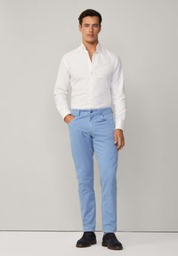 Weißes Hemd mit Knöpfen, hellblaue Hose und dunkle Schuhe. Einfaches Design mit maßgeschneiderter Passform, keine sichtbaren Muster oder Akzente.