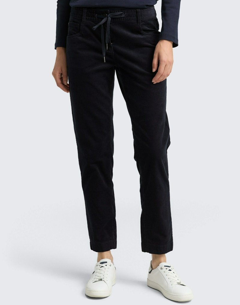Pantalons en velours côtelé bleu marine avec une taille élastiquée et des poches, présentant une jambe fuselée et un tissu texturé, assortis à des baskets blanches.