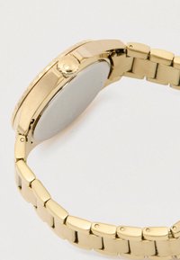 Gold metal wristwatch shown from side with linked bracelet and crown on case against white background.