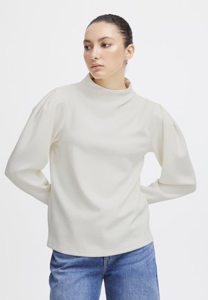 Haut crème à manches longues avec un col montant et des manches bouffantes, en tissu lisse et léger. Ourlet droit et coupe décontractée.