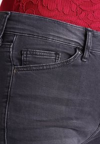 Mörkgrå denimjeans med en jämn textur, med en liten framficka, bältesöglor och sydda detaljer längs sömmarna.