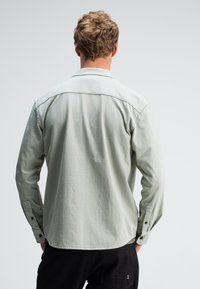 Lichtgroen overhemd met lange mouwen, knopen bij de manchetten en een achterpand met een yoke-ontwerp. Zacht, textuurstof met een ontspannen pasvorm.