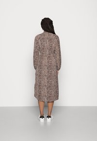 Šaty s leopardím vzorem, dlouhými rukávy a stahovacím pasem, délka ke středu lýtek a měkký materiál; zkombinované s elegantními bílými teniskami.