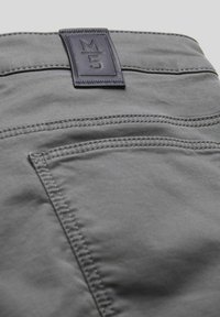 Graue Stoffhosen mit glatter Textur, versehen mit einem rechteckigen blauen Lederpatch mit der Aufschrift "M5" und sichtbaren Nähdetails.
